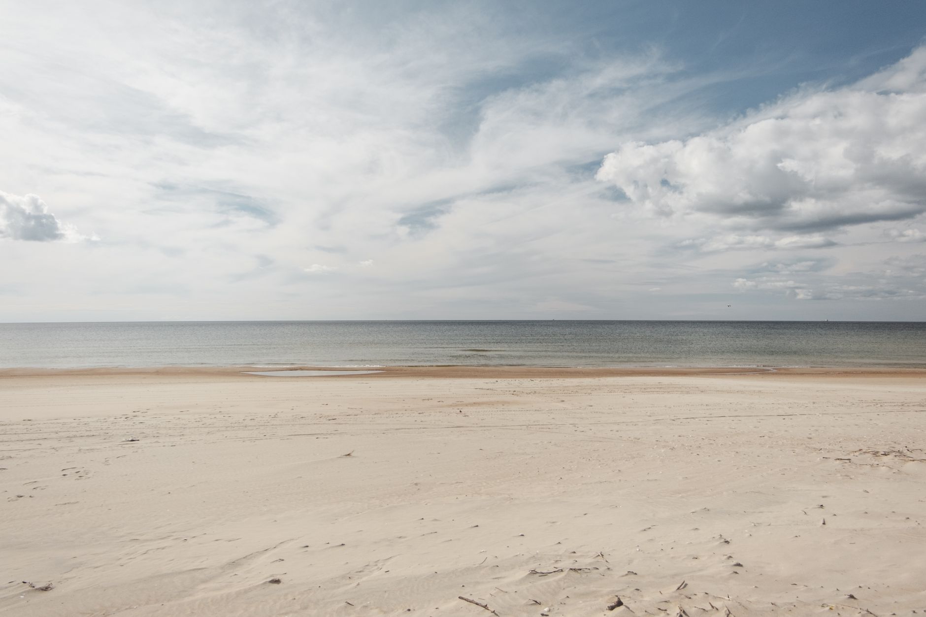 En bred sandstrand ved havet under en let skyet himmel
